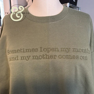 Olive green sweatshirt with embroidered quote about mother on front, displayed on mannequin in store
