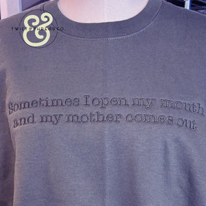 Dark gray crewneck shirt with embroidered text saying sometimes I open my mouth and my mother comes out