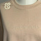 Beige crewneck sweatshirt with embroidered text 'overstimulated.' on chest and Twist & Thread Co. logo