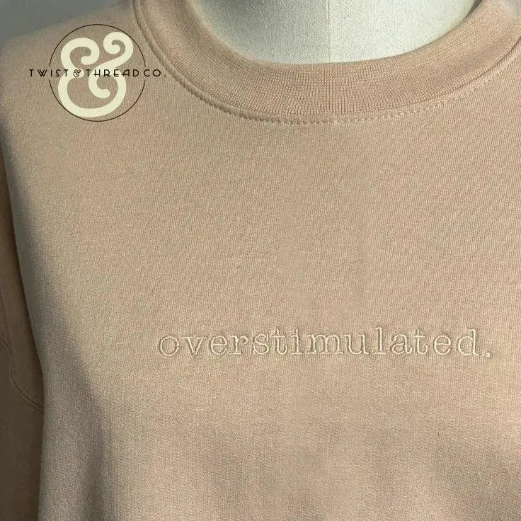 Beige crewneck sweatshirt with embroidered text 'overstimulated.' on chest and Twist & Thread Co. logo