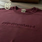 Maroon Gildan sweatshirt with embroidered word 'overstimulated' on chest, laid on wooden surface