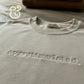 Close-up of a white Gildan sweatshirt with embroidered word 'overstimulated' on a wooden surface