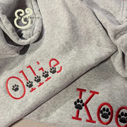 Gray dog hoodie with custom red embroidered text 'Ollie' and black paw prints, Twist & Thread Co. logo