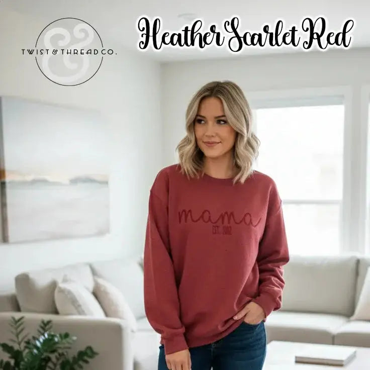Woman wearing heather scarlet red "mama EST. 2012" sweatshirt in bright living room with white couch