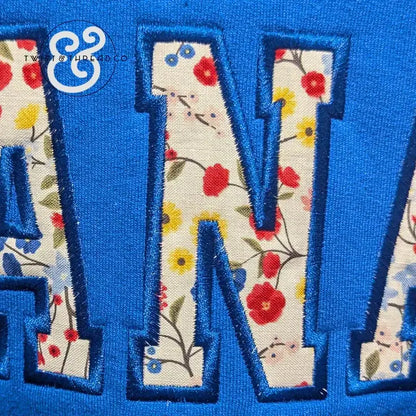 Blue fabric with floral patterned applique letters forming part of the word 'MAMA'