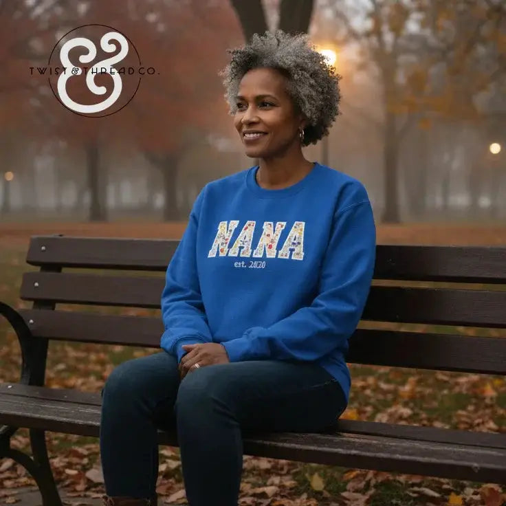 Smiling woman wearing blue Nana est. 2020 sweatshirt sitting on park bench in autumn