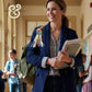 Teacher smiling in school hallway with backpack adorned by colorful teacher-themed bag tag and holding books