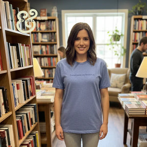 Smiling woman in blue t-shirt with "I read past my bedtime" text standing in cozy bookstore with shelves and books