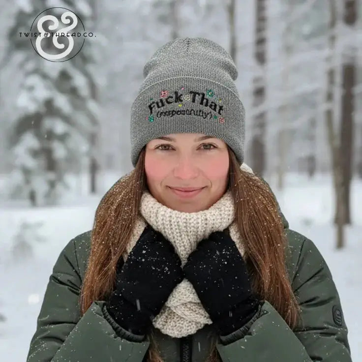 Woman in snowy forest wearing gray beanie with text, green winter jacket and cream scarf