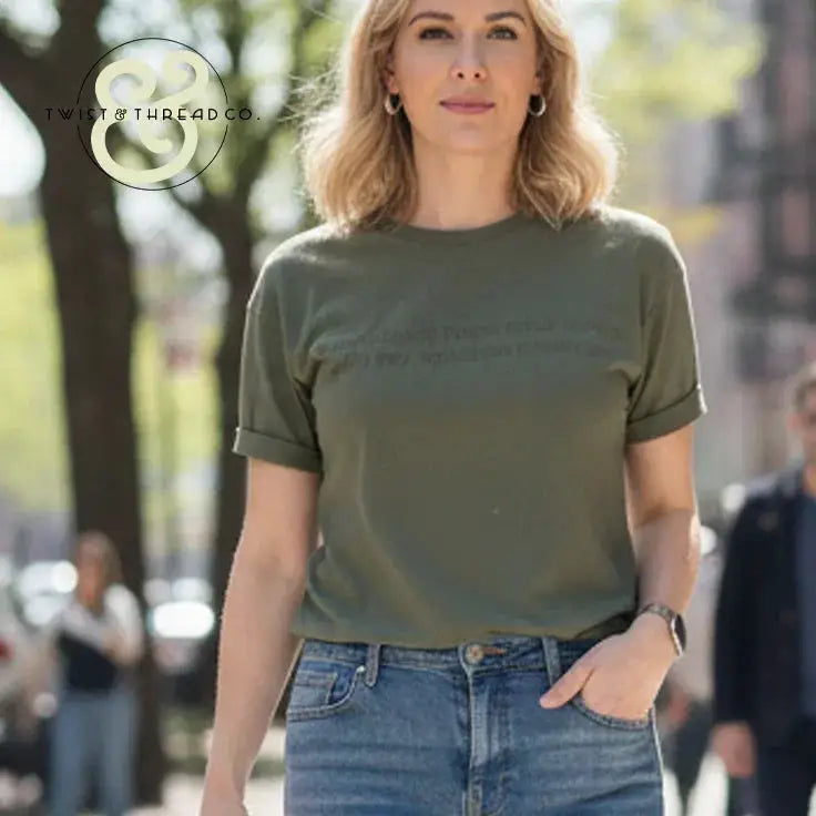 Woman wearing green graphic tee and blue jeans standing outdoors in city street with trees