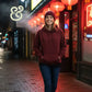 Smiling woman wearing maroon hoodie and beanie walking on a lit urban street with red lanterns at night