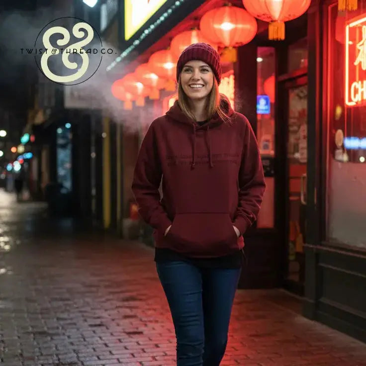 Smiling woman wearing maroon hoodie and beanie walking on a lit urban street with red lanterns at night