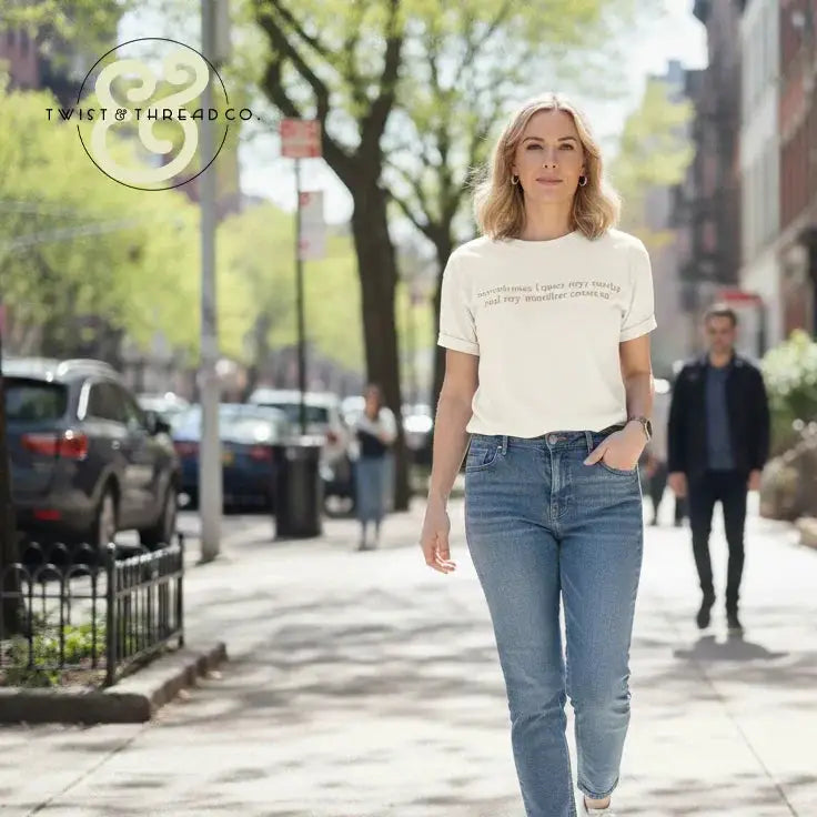 Woman walking on sunlit city sidewalk wearing white graphic tee and blue jeans, urban street scene