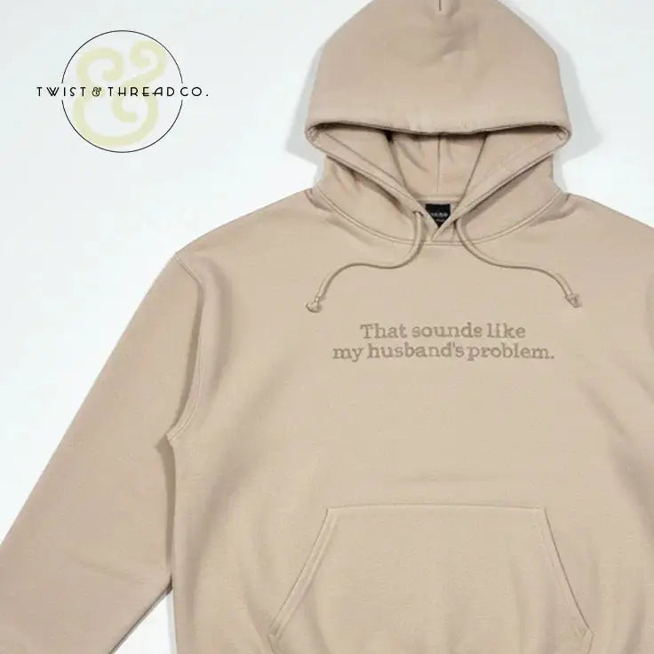 Beige hoodie with front pocket and text That sounds like my husband's problem embroidered on chest