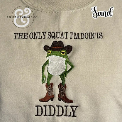Sand-colored fabric with embroidered green frog wearing brown cowboy boots and hat, text 'The only squat I'm doin' is diddly'