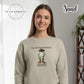 Young woman wearing sand-colored sweatshirt with cartoon frog in cowboy hat and boots, text design