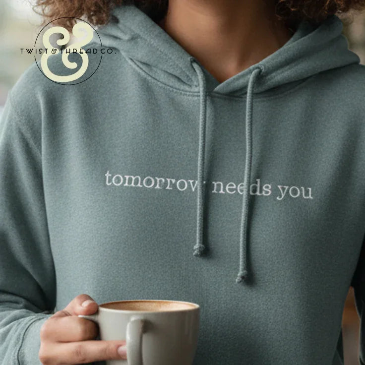 Custom embroidered hoodie with 'tomorrow needs you' text, Twist & Thread Co. branding, coffee mug