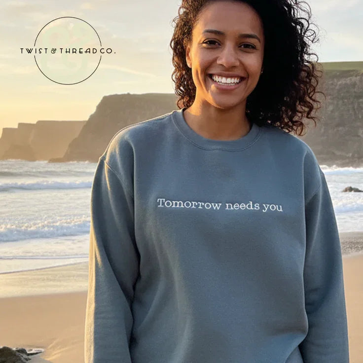 Smiling woman on beach wearing custom embroidered 'Tomorrow needs you' sweatshirt by Twist & Thread Co.