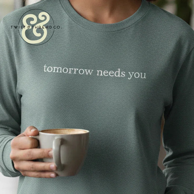 Custom embroidered hoodie with 'tomorrow needs you' text, Twist & Thread Co. branding, person holding mug