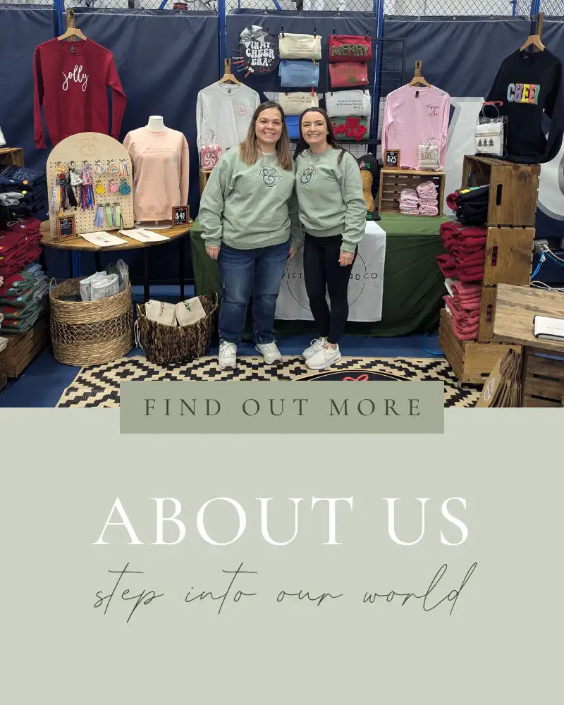 Two women in matching light green sweatshirts with a small embroidered logo stand together at an outdoor market stall.