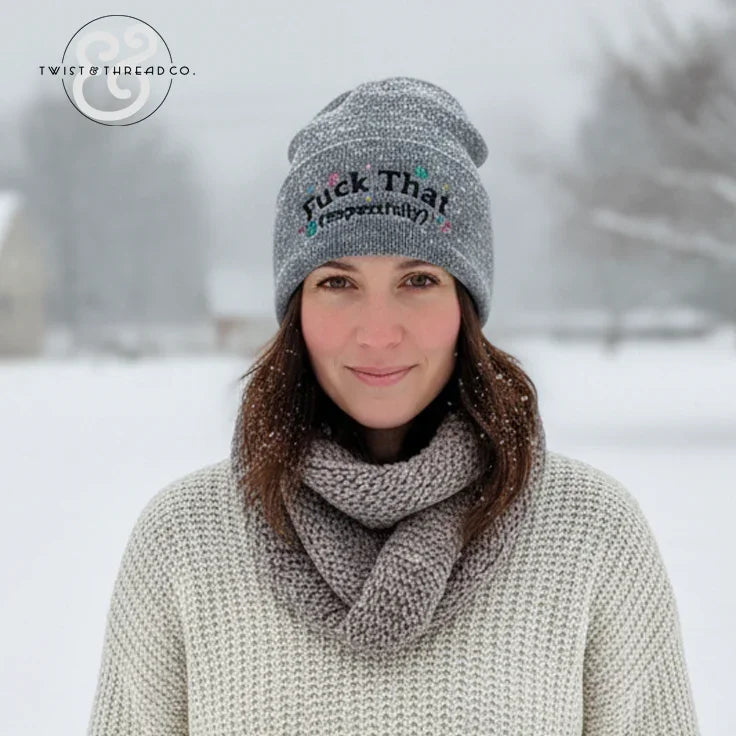Woman wearing grey knit winter hat with embroidered text, scarf, and sweater in snowy outdoor setting