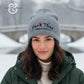 Woman in gray embroidered winter hat with text, outdoors in snowy setting