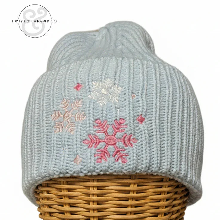 Light blue knit winter hat with pink and white snowflake embroidery on a wicker stand