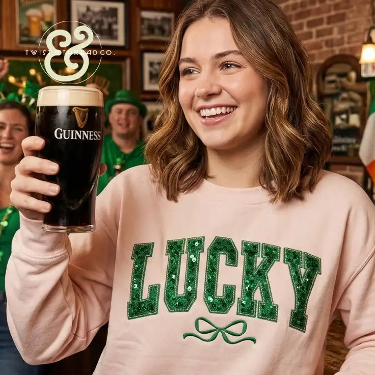 A woman wearing a pink sweatshirt with the word ’lucky’ in green sequined letters and an embroidered bow beneath it.